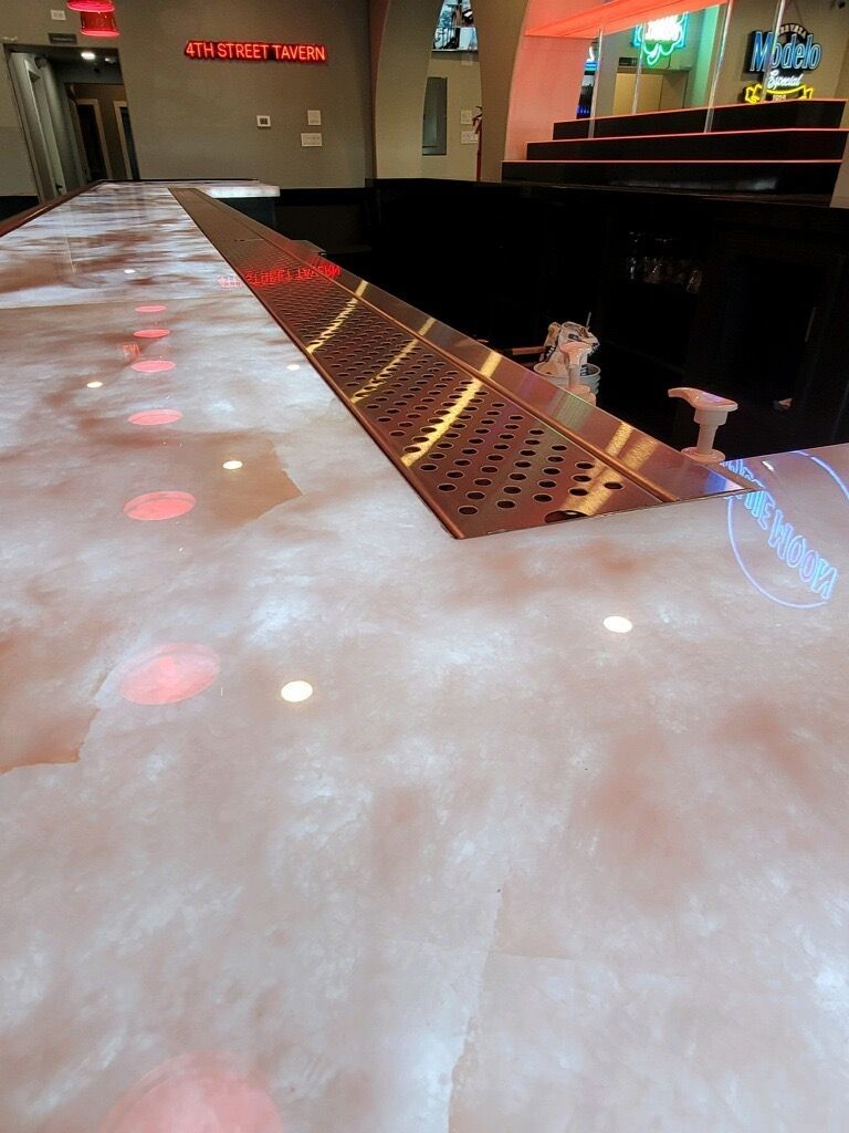 Bar with white countertop, metal drain, and red lights. Dark interior, stairs visible in the background.