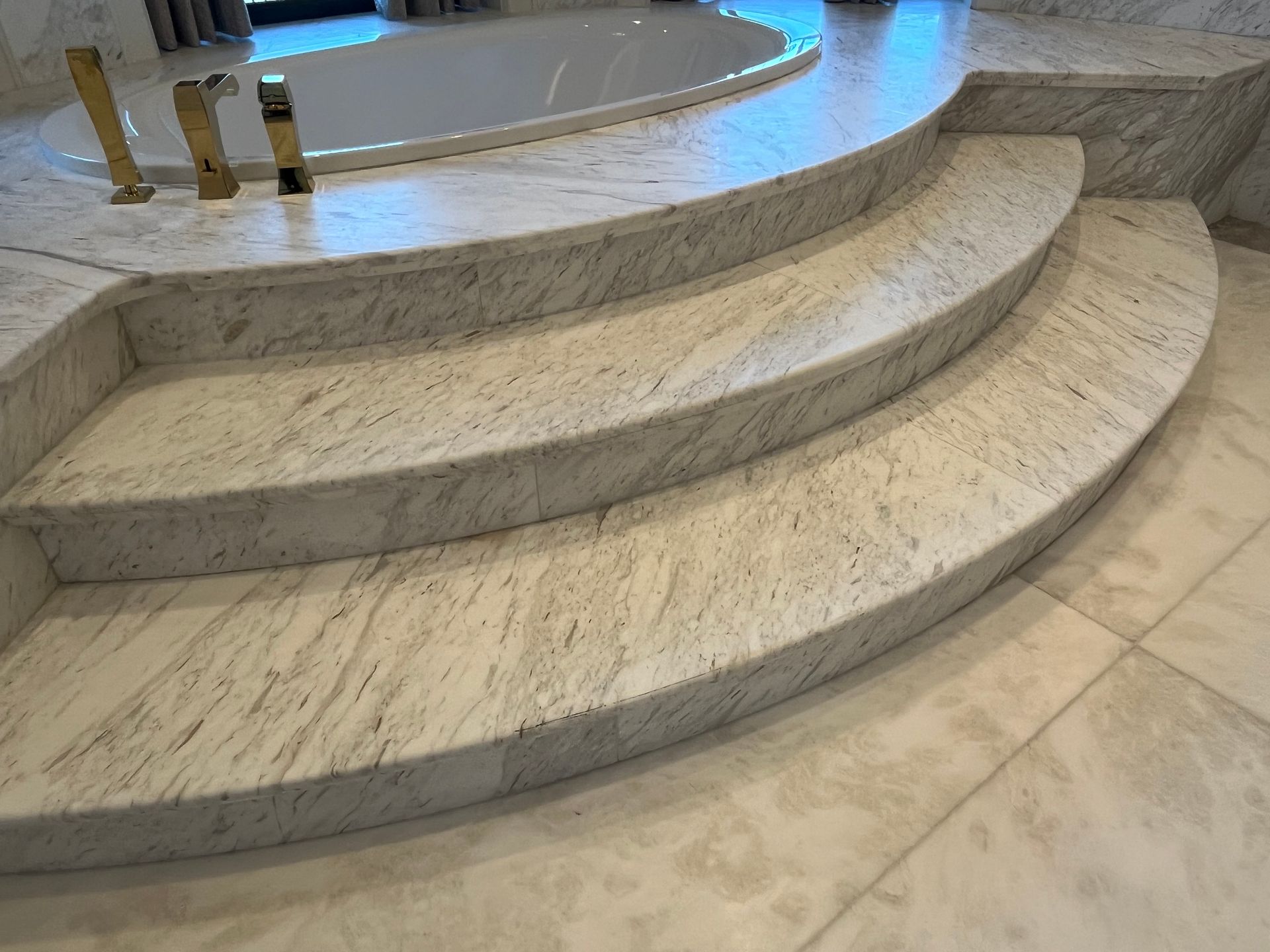 Marble steps leading up to a bathtub. Gold fixtures are visible.