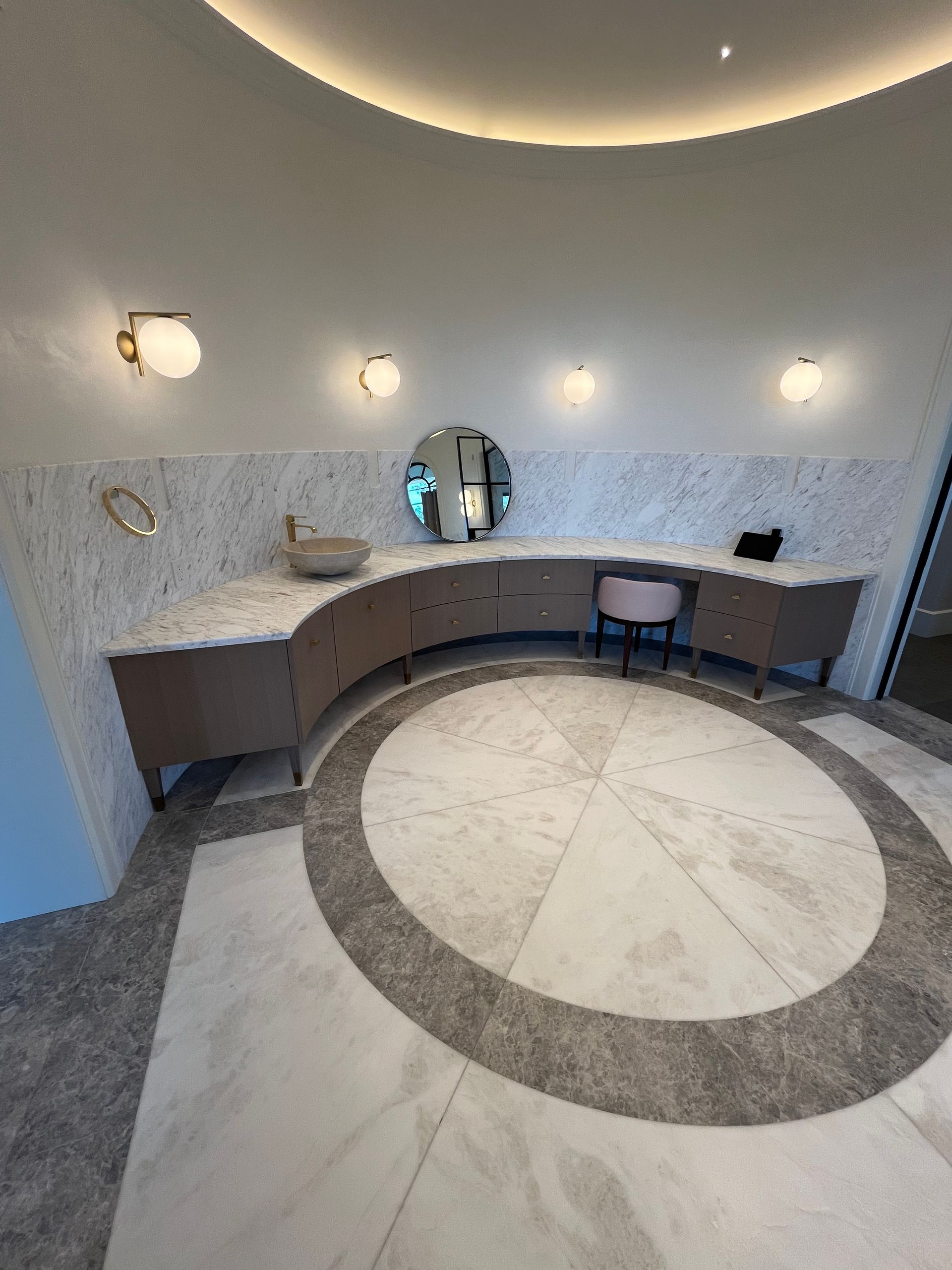 Curved vanity in a modern bathroom, featuring a round mirror, marble backsplash, and patterned floor.