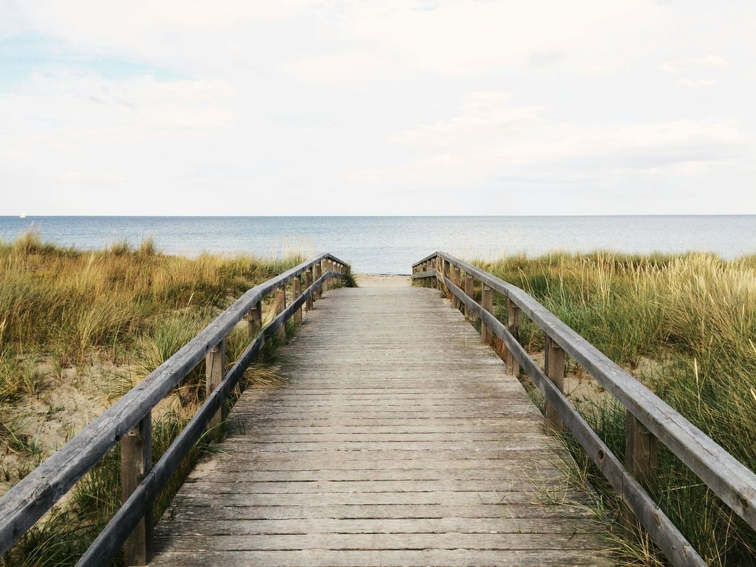 Wooden boardwalk leading through dunes to a calm ocean under a pale sky