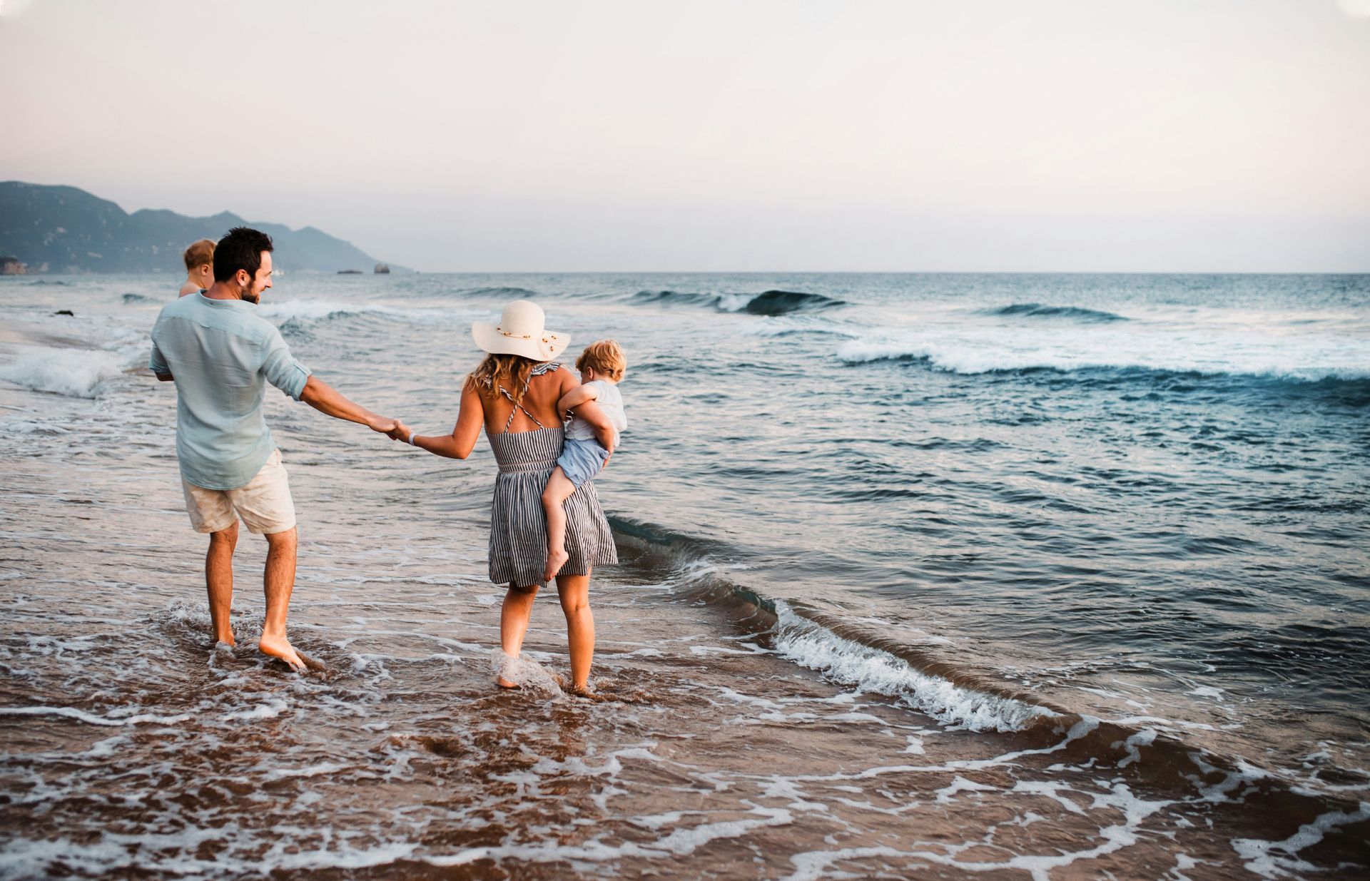Two people holding hands and walking along a beach at sunset, waves washing the shore