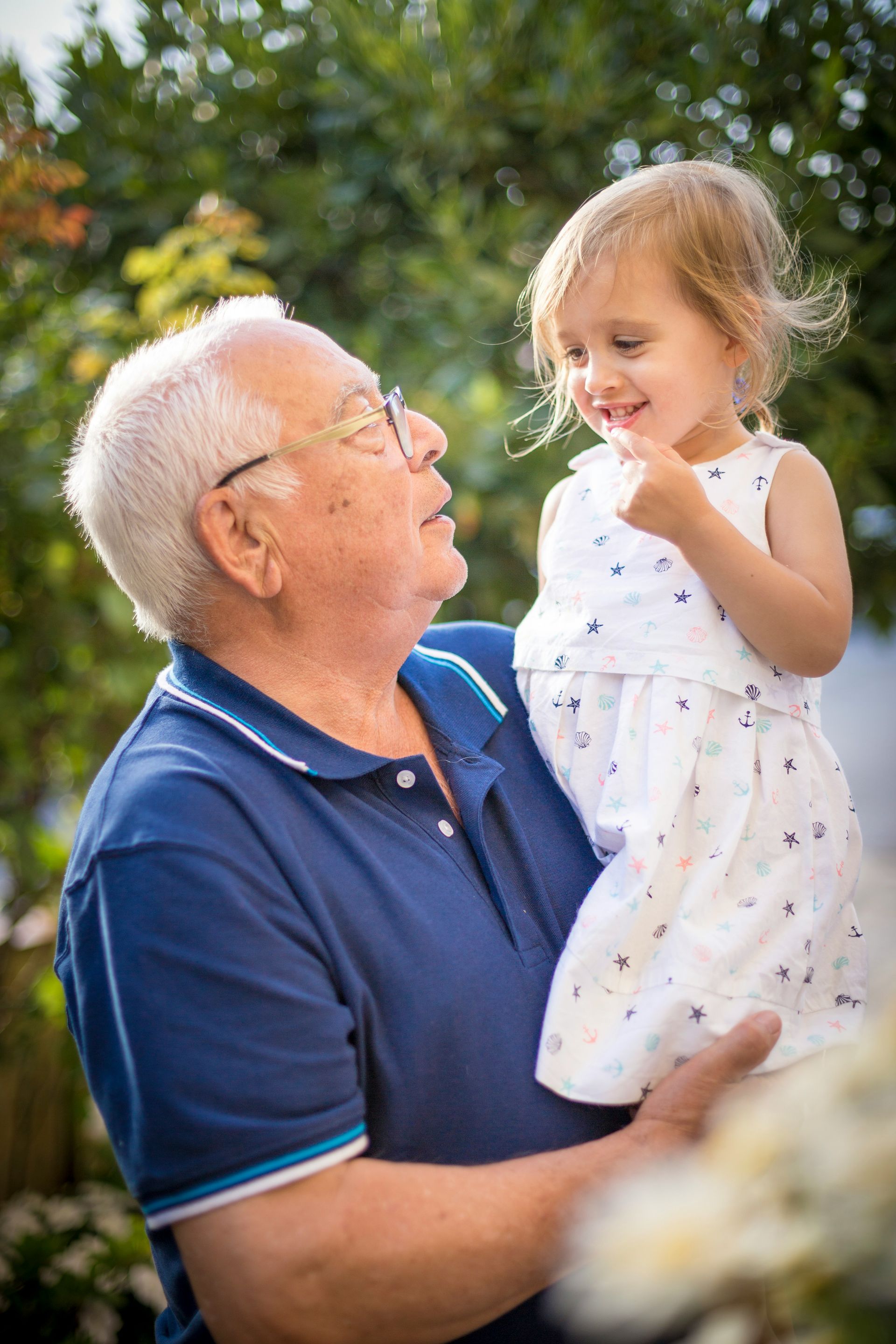 Elderly man in a blue polo holding a smiling child outdoors in a garden