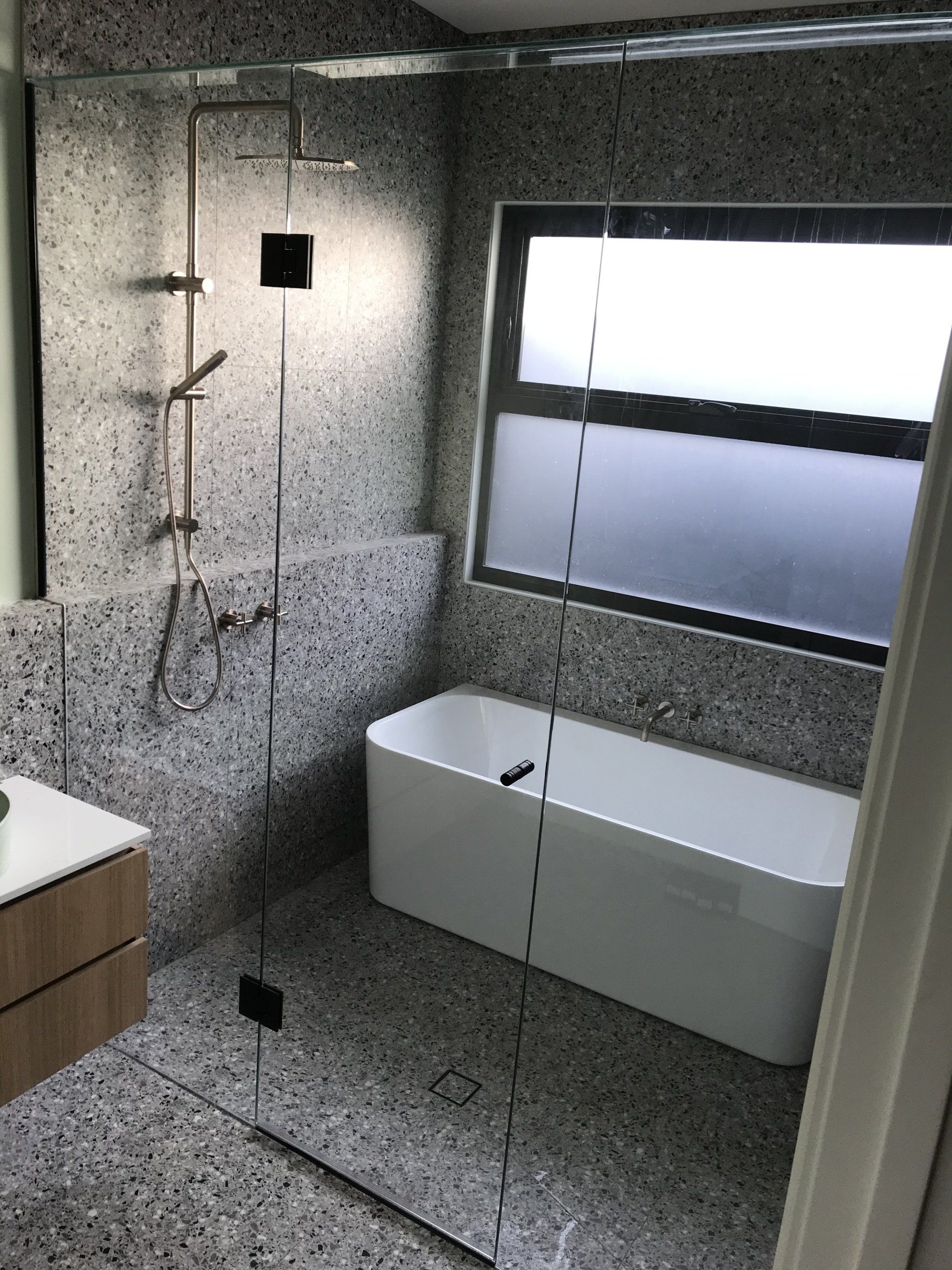 A bathroom with a bathtub , Frameless Hinged Shower Screen and mirror.