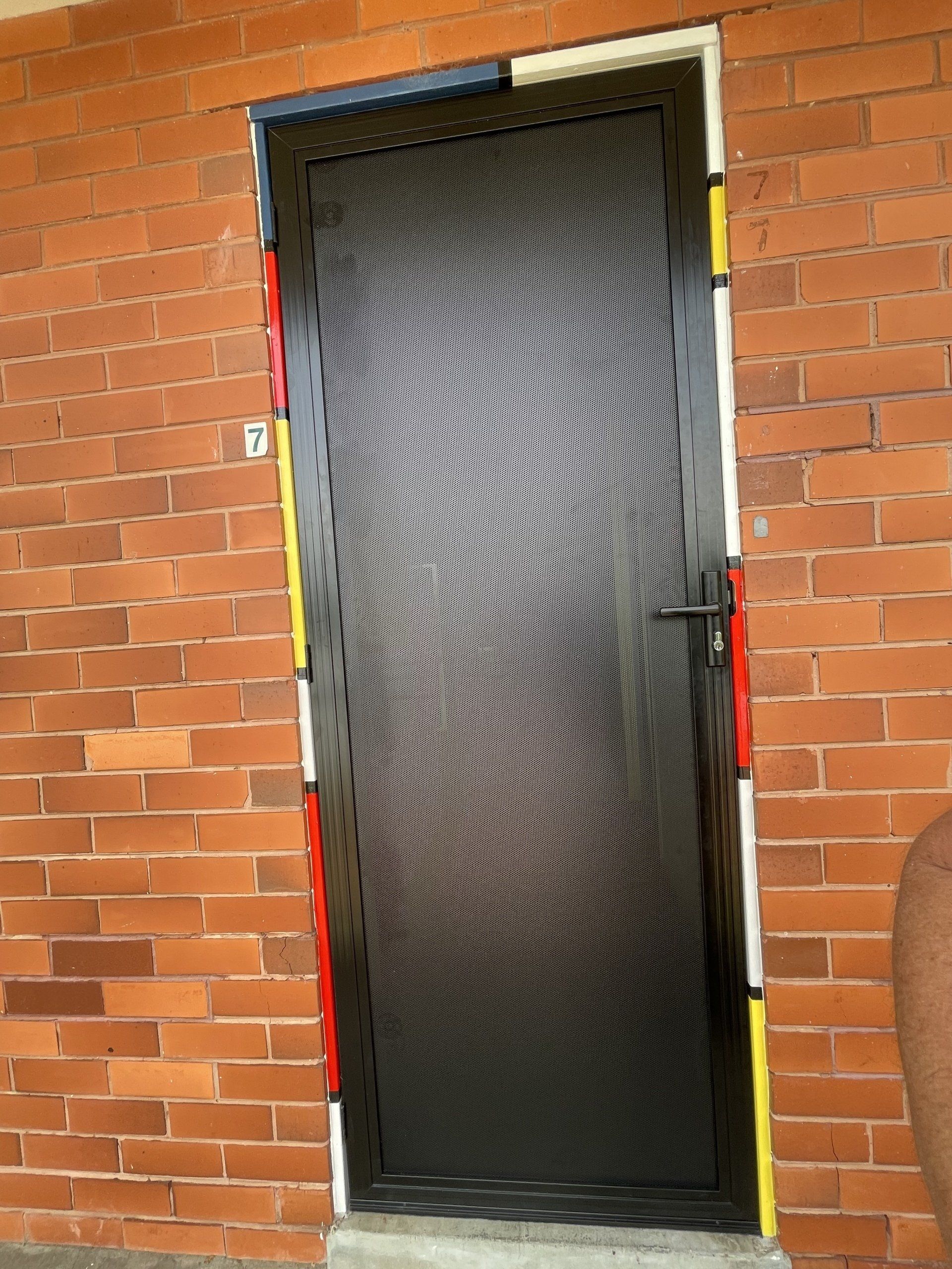 A black Security Door is sitting on a brick wall.