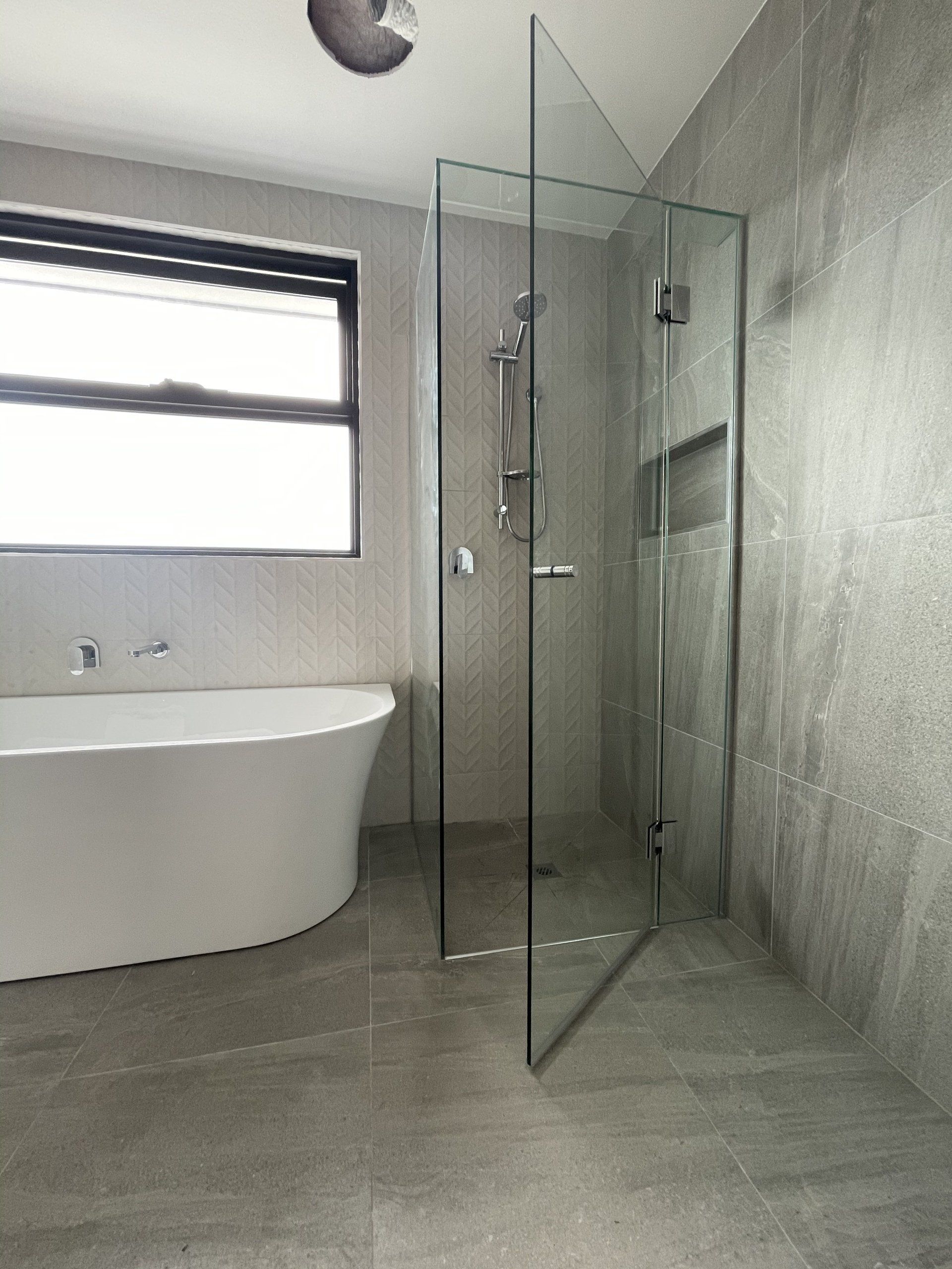 A bathroom with a bathtub , Frameless Hinged Shower Screen , and window.