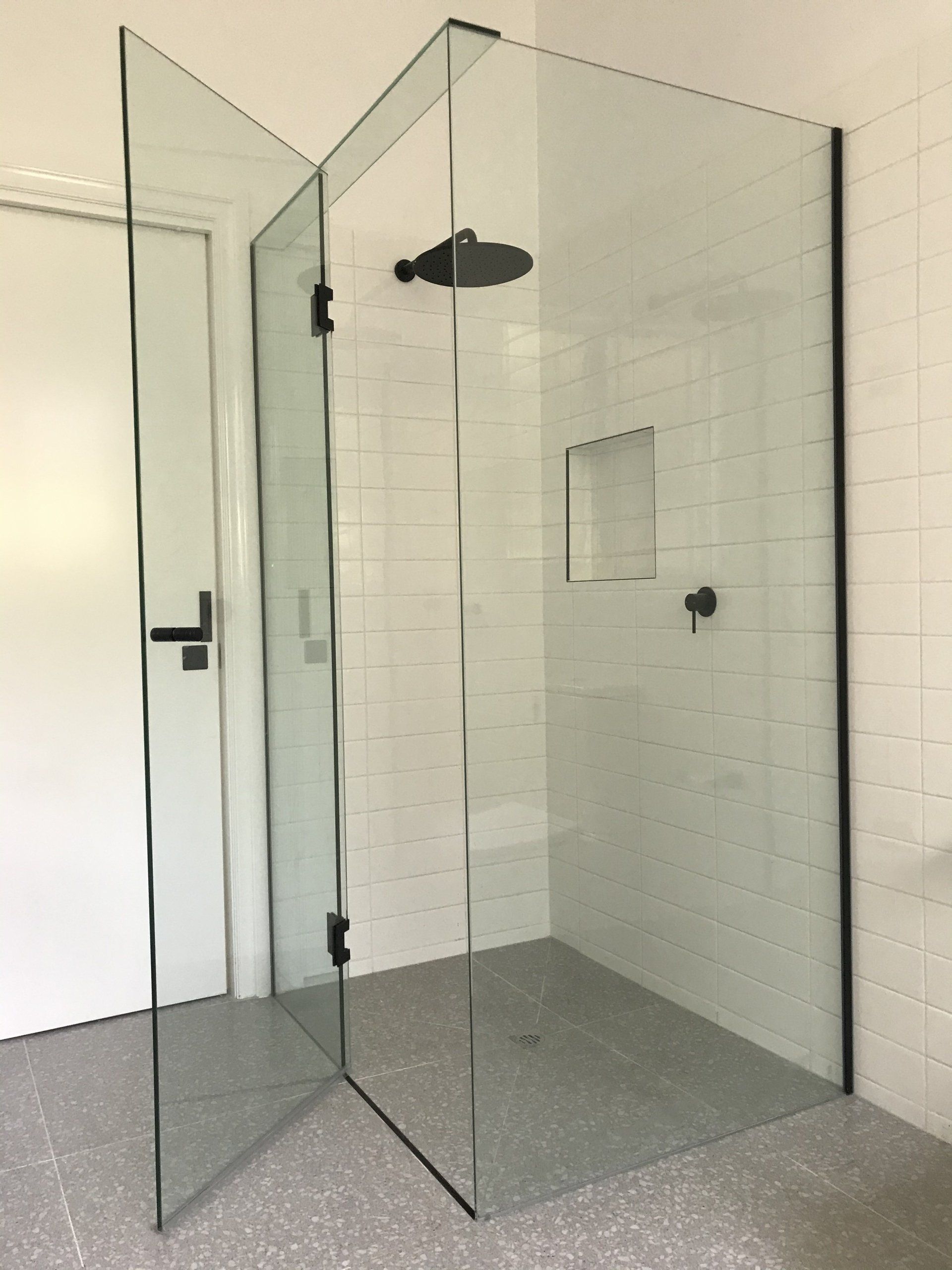 A bathroom with a walk in shower with a black shower head.