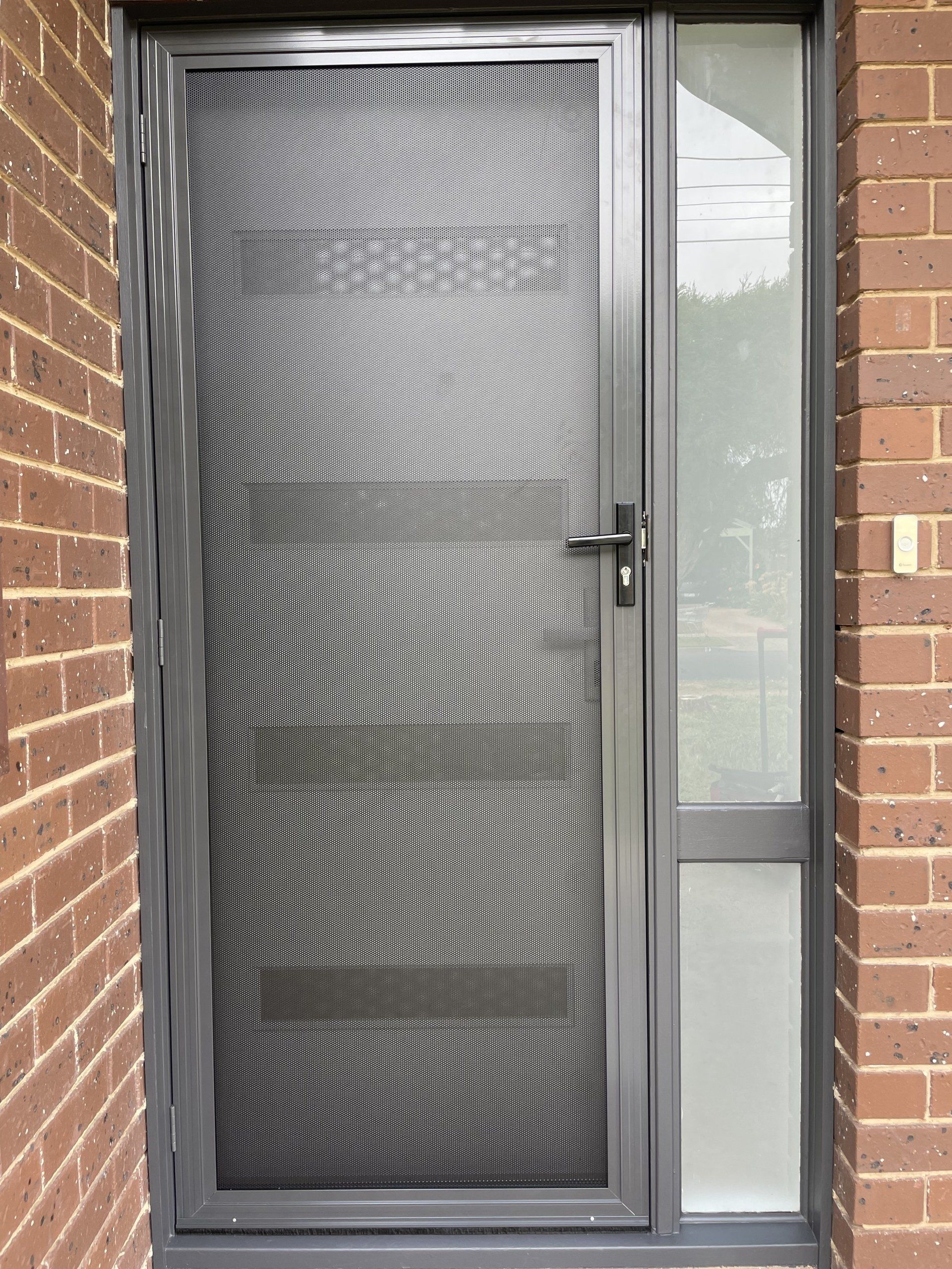 A black Security Door with a screen on it is on a brick wall.
