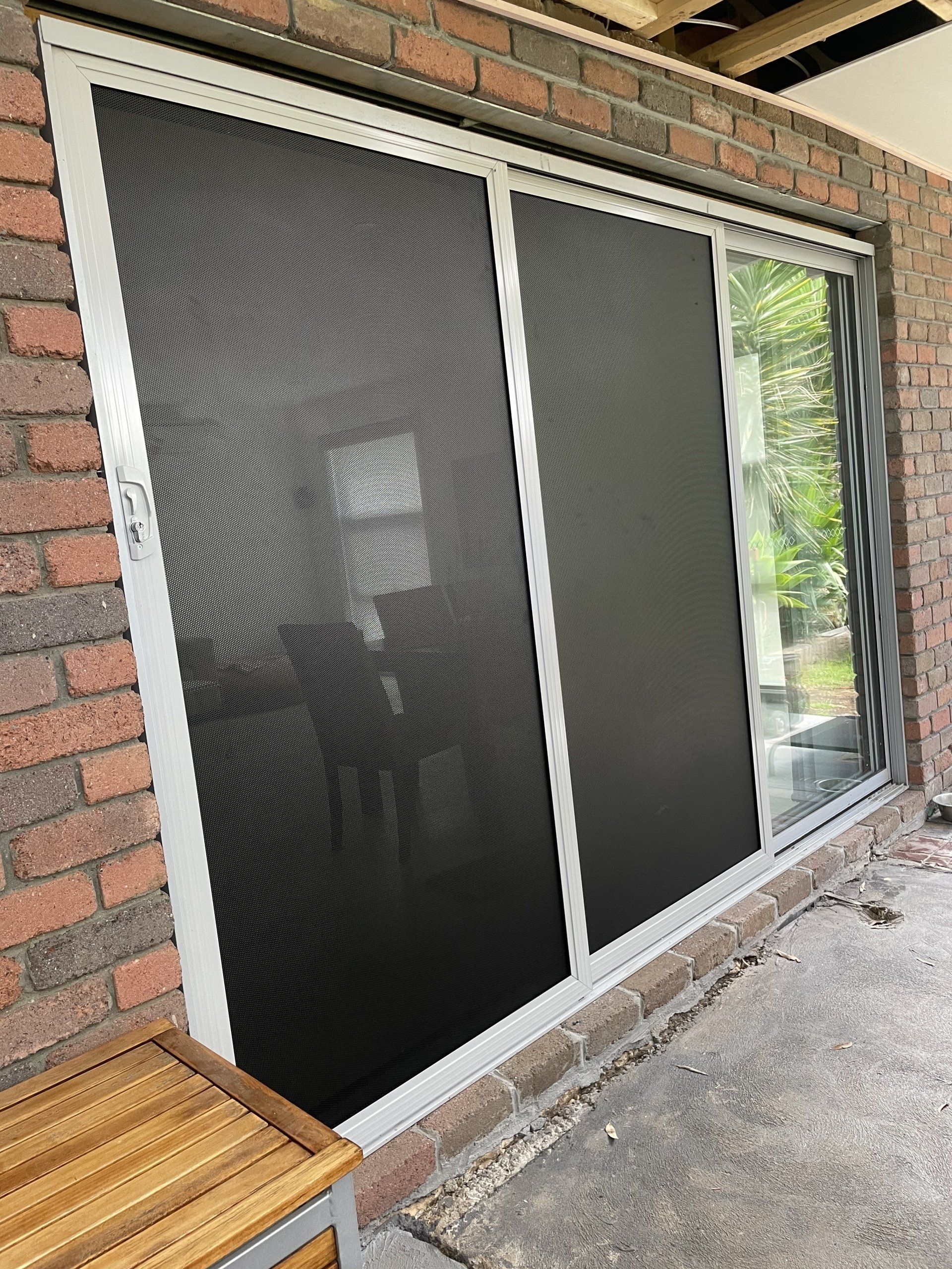 A sliding Security Door with a screen on it is on a brick wall.