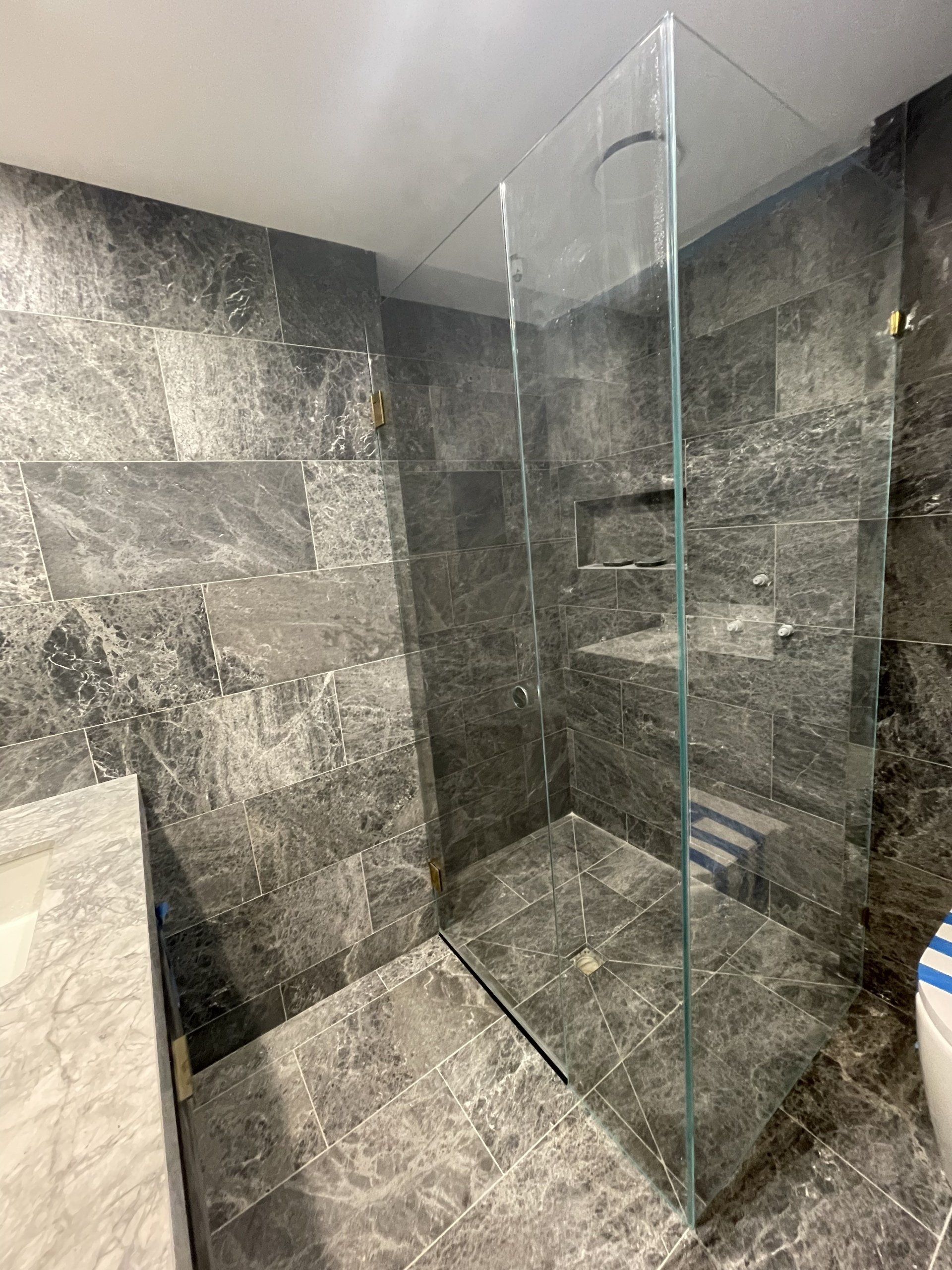 A bathroom with marble tiles and a walk in Frameless Hinged Shower Screen with a glass door.