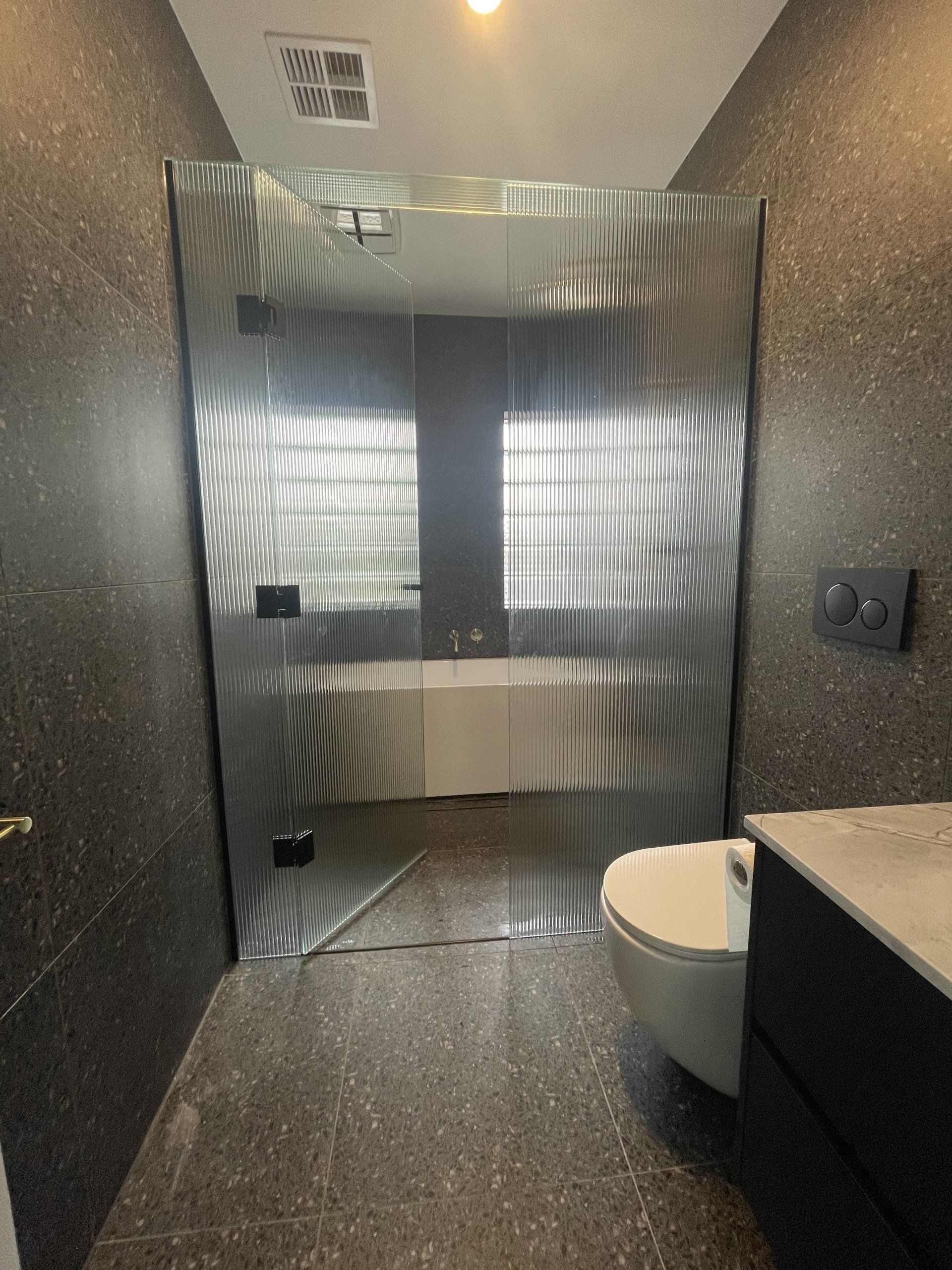A bathroom with a toilet , bathtub and Frameless Hinged Shower Screen stall.