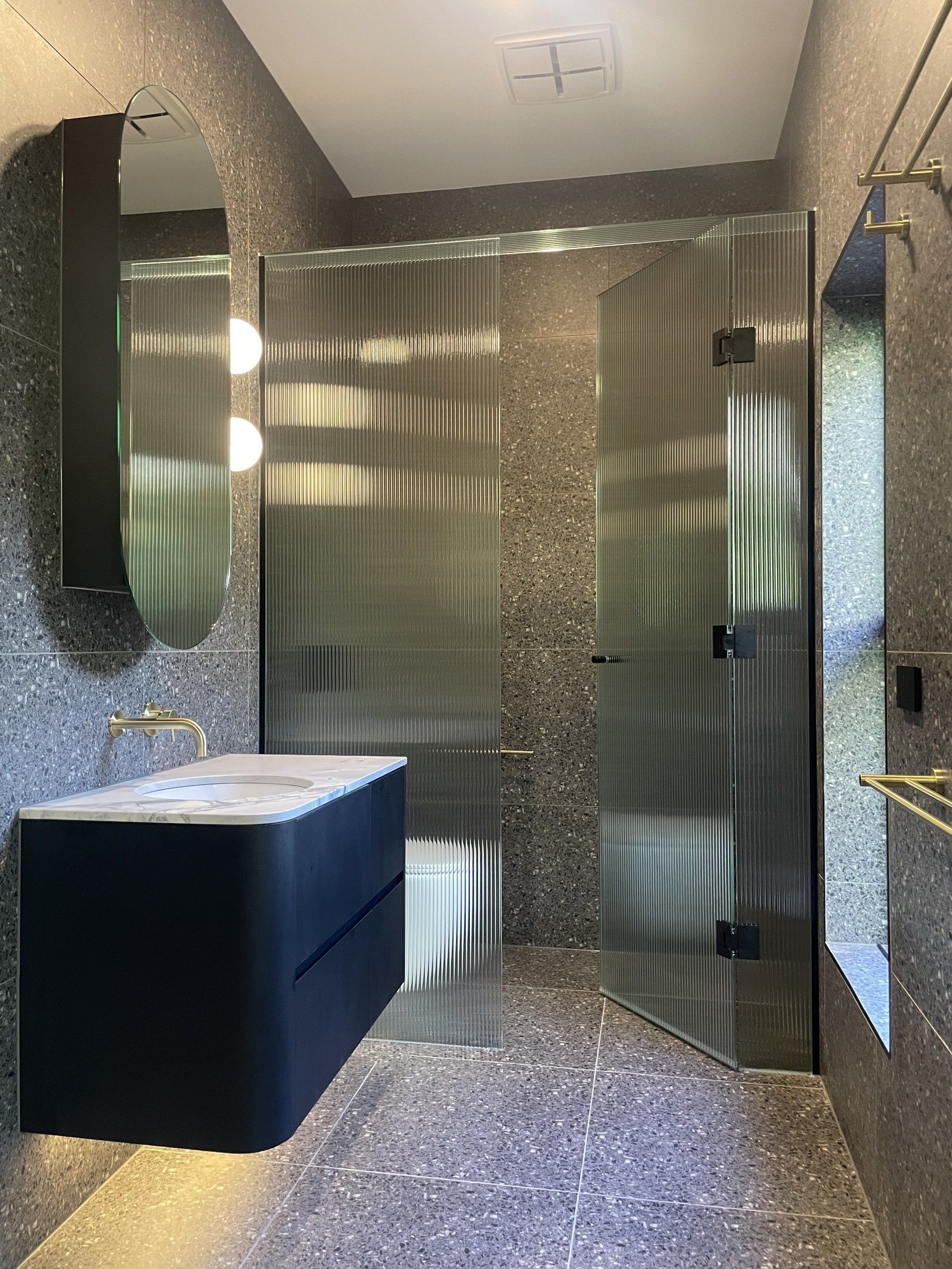 A bathroom with a sink , toilet , Frameless Hinged Shower Screen and mirror.