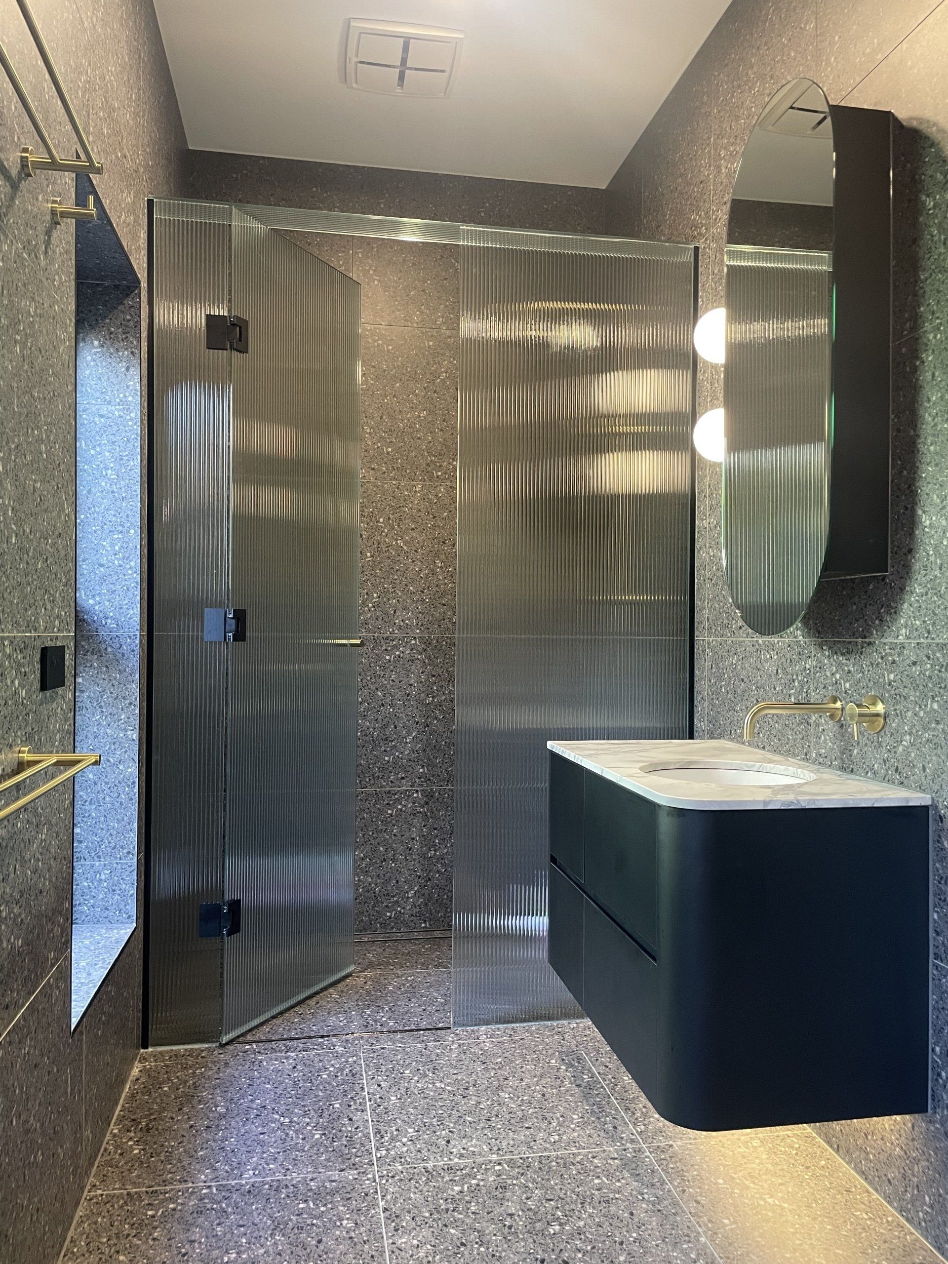 A bathroom with a sink and a walk in Frameless Hinged Shower Screens.