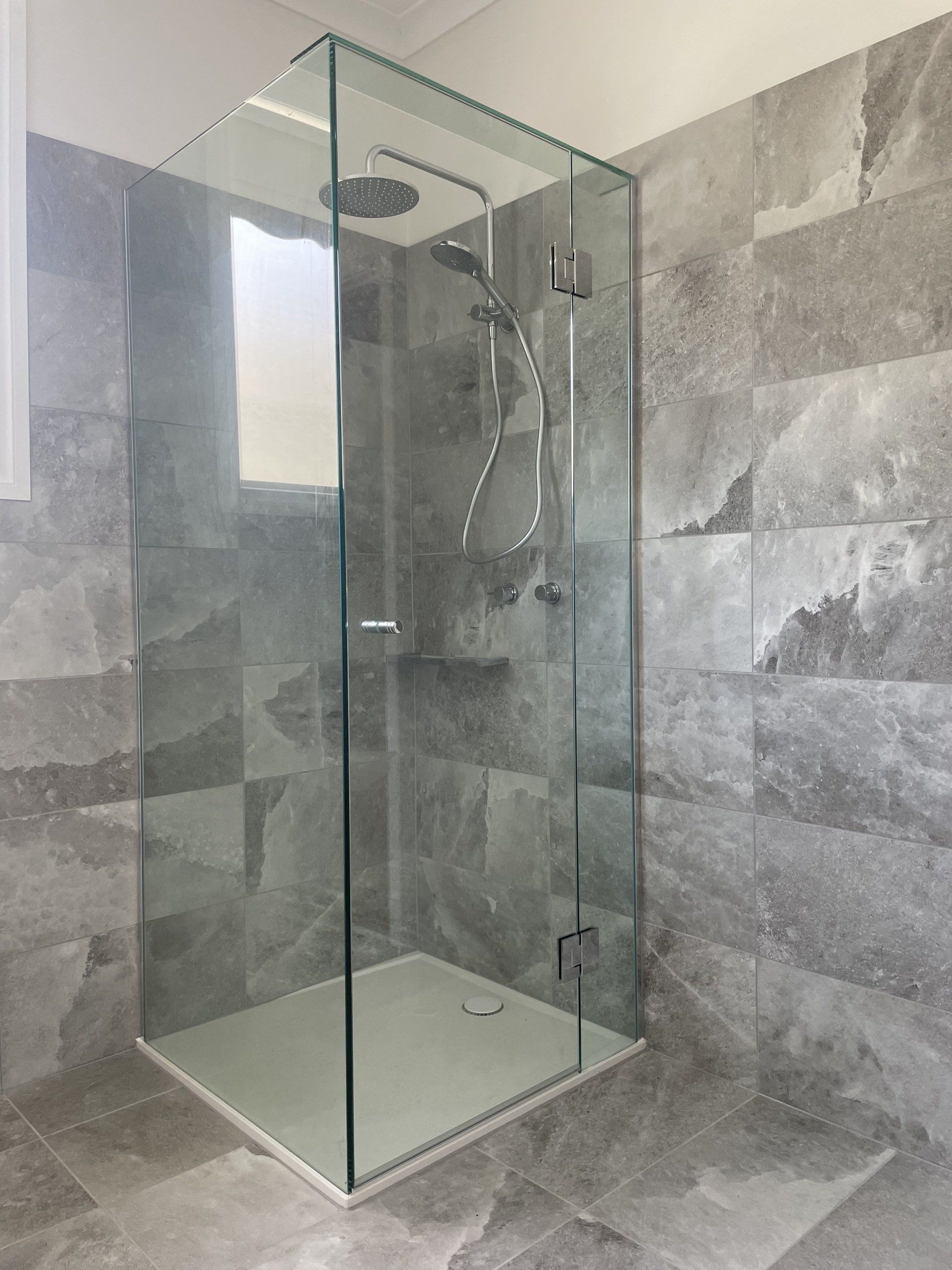 A bathroom with a walk in Frameless Hinged Shower Screen with a glass door.