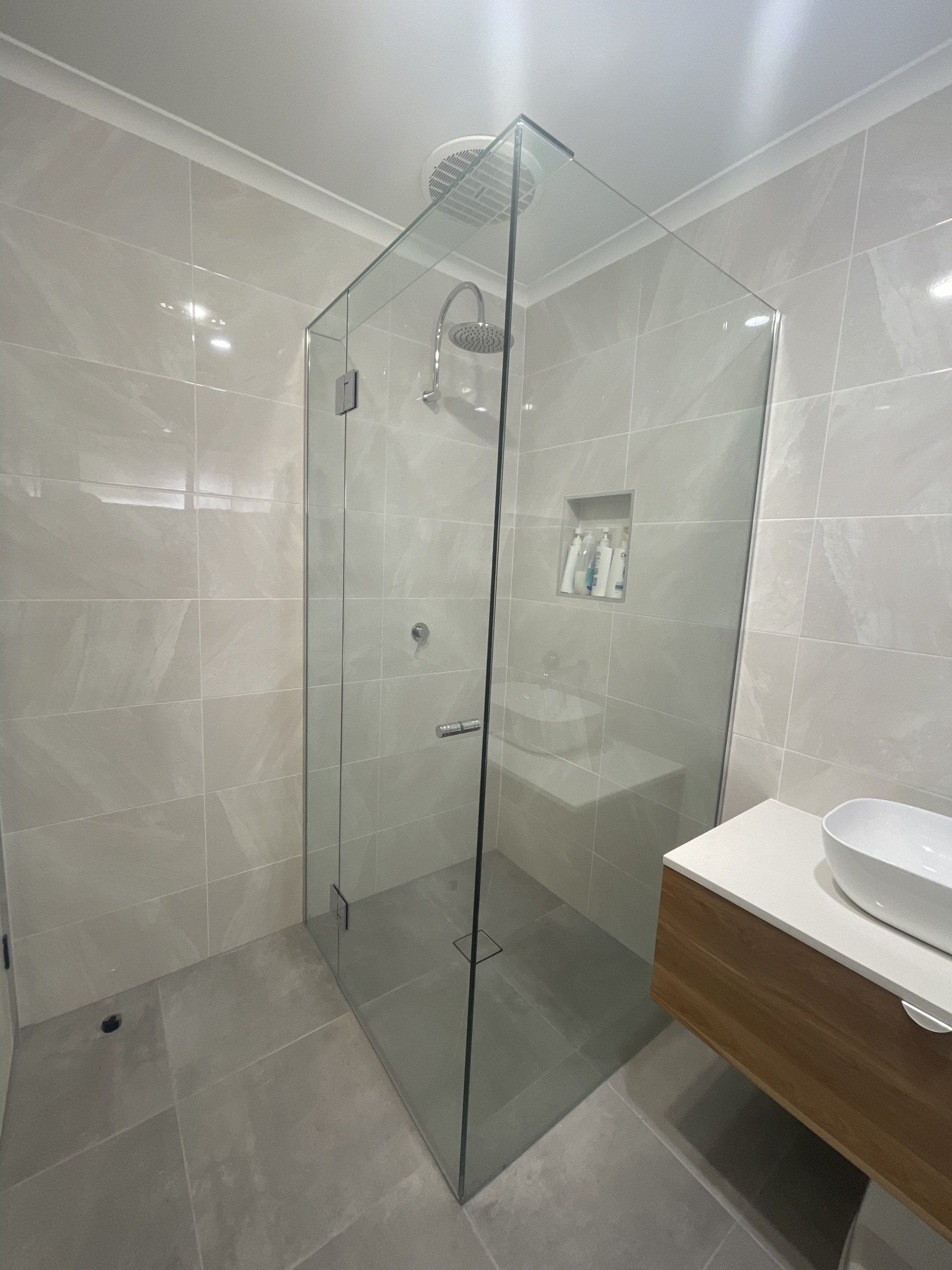 A bathroom with a walk in Frameless Hinged Shower Screen and a sink.