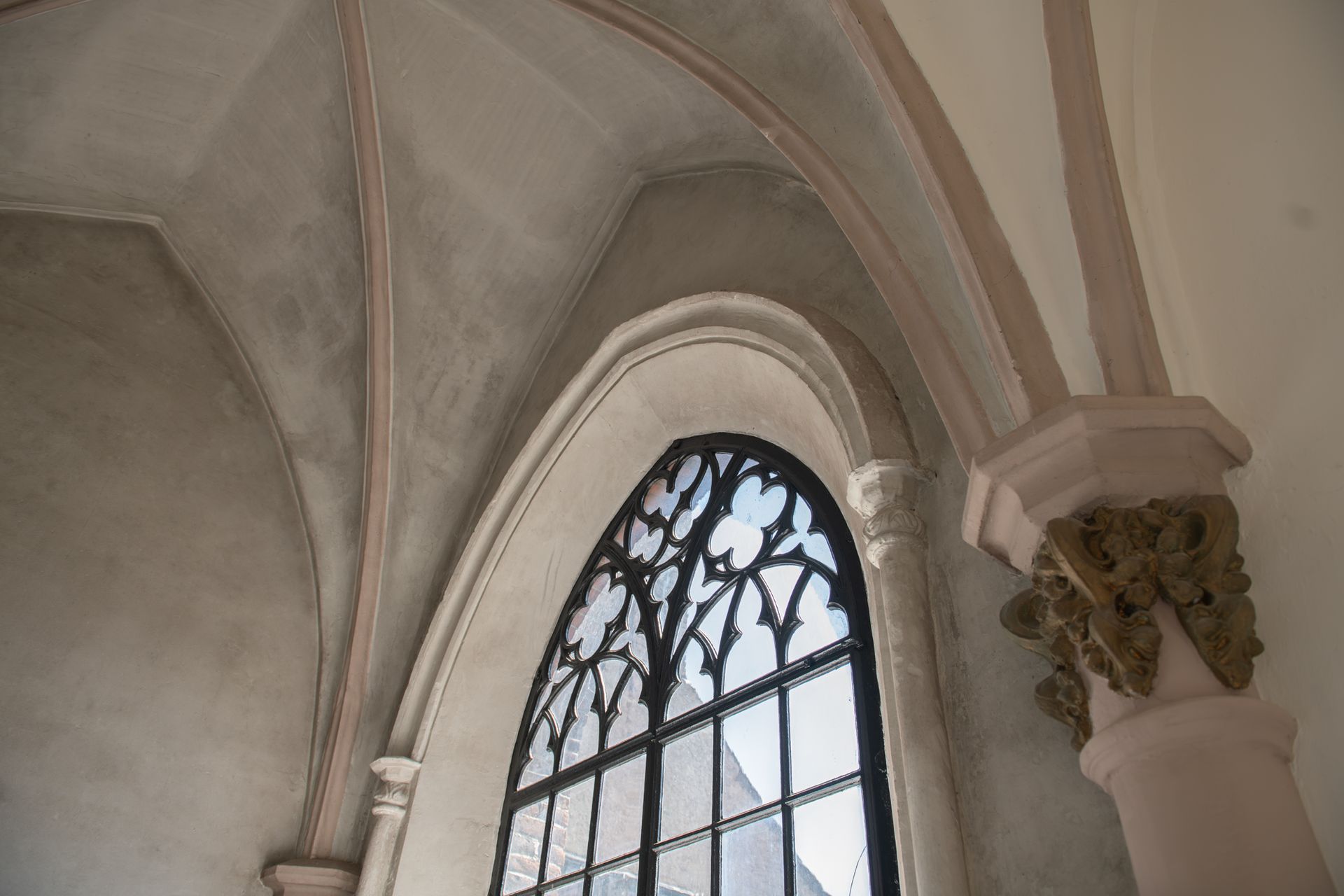 Een gewelfd plafond met stenen ribben die samenkomen bij een gotisch venster en een sierlijk pilaarkapiteel.