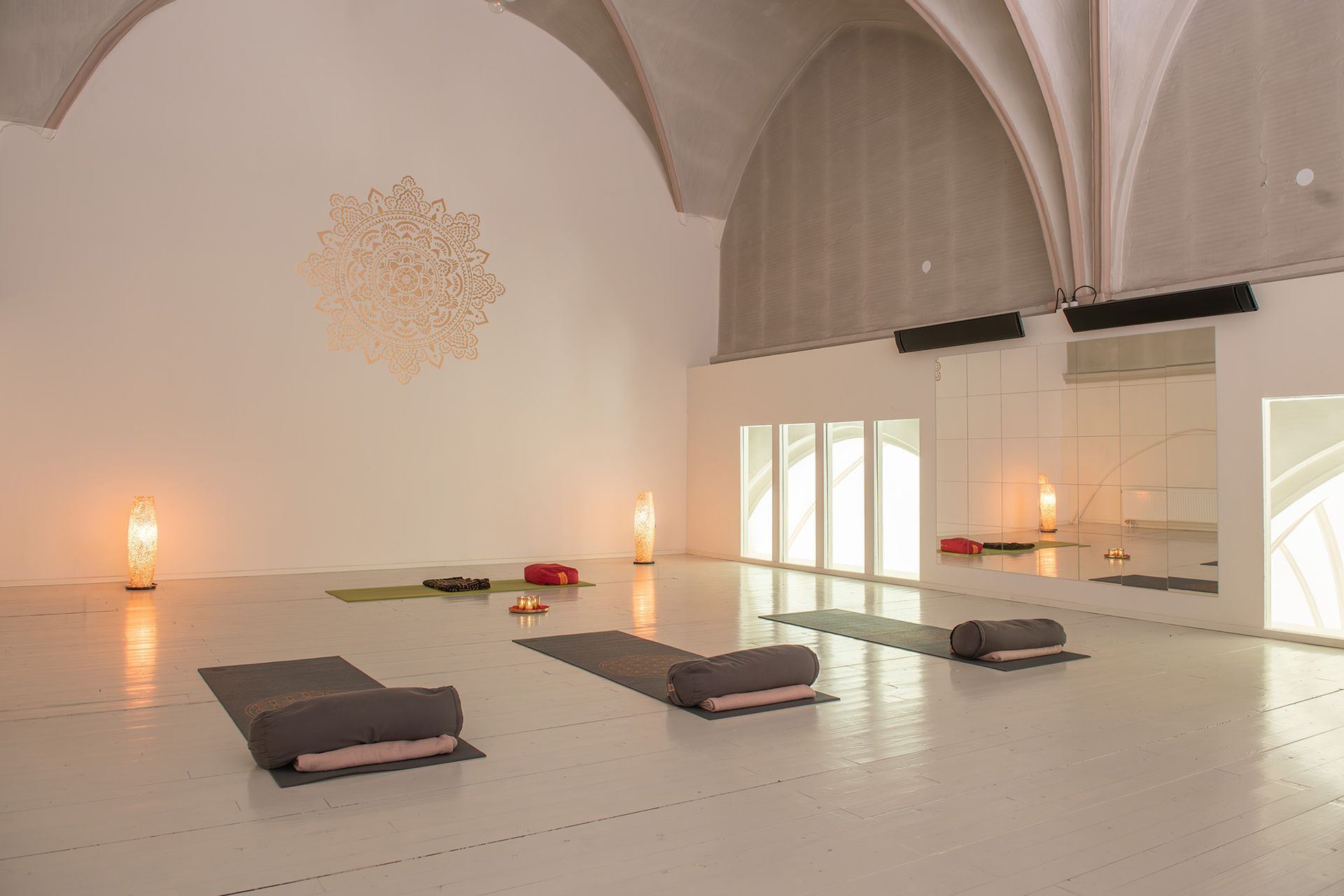 Een minimalistische, helder verlichte yogastudio met hoge gewelfde plafonds, witte vloeren, yogamatten en warme, sfeervolle vloerlampen.