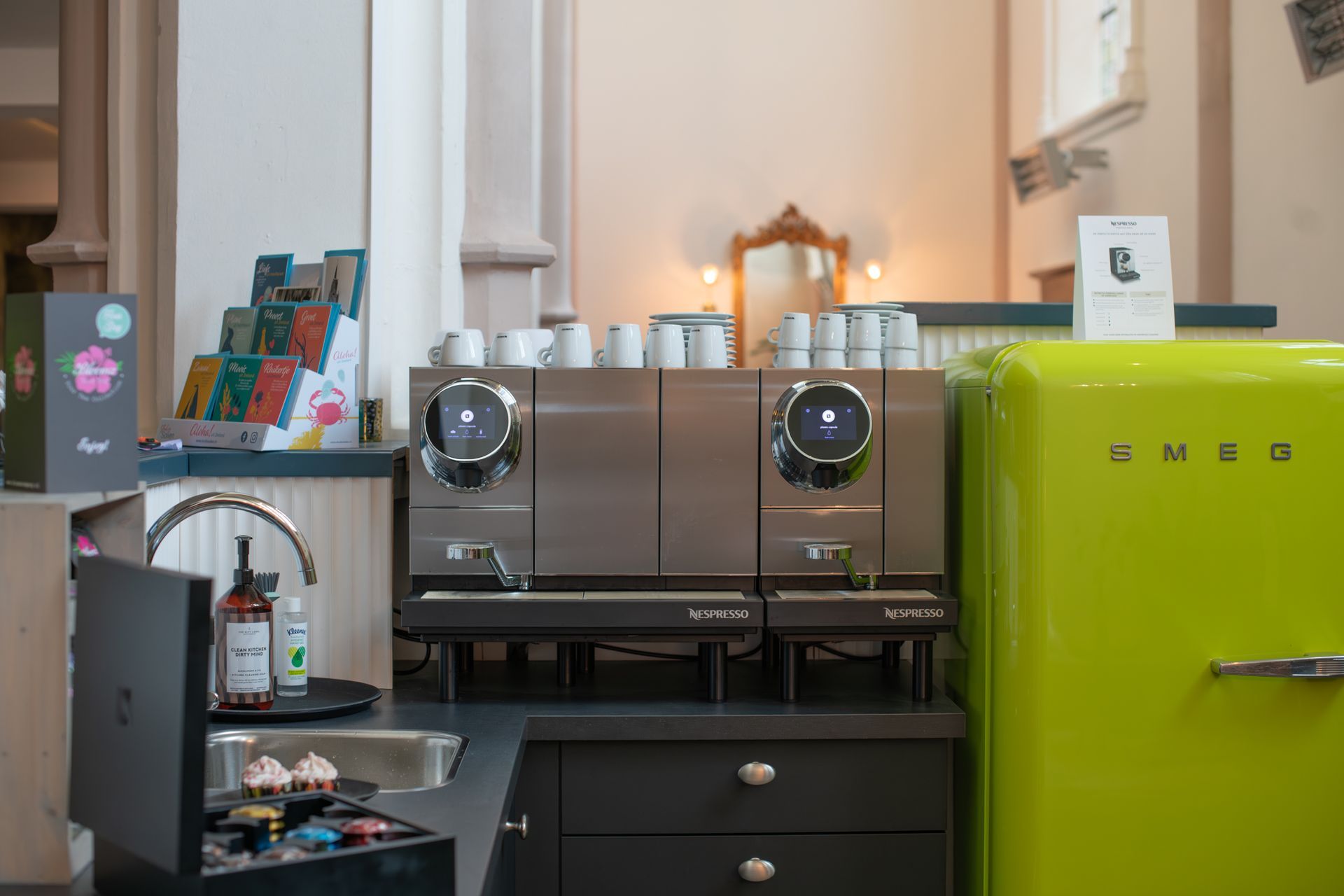 Een koffiehoek met een professionele espressomachine, witte mokken en een felgroene Smeg-koelkast op een donker aanrecht.