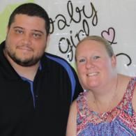 Two smiling people posing in front of a wall with decorative script and hearts