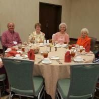 Four people seated at a banquet table with red napkins in a conference room.