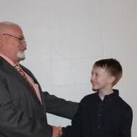 Two people shaking hands indoors, both smiling and facing each other.