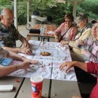 People gathered around a picnic table outdoors, sharing food and drinks under a covered patio.