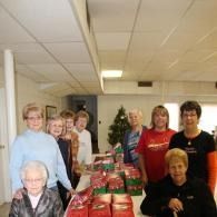 Group of people standing behind stacks of red gift bags in a bright community room