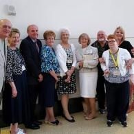 Group of people standing indoors, posing for a photo against a plain wall.