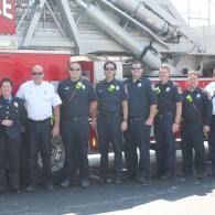 Group of firefighters and responders standing in front of a fire truck, posing together in uniform.