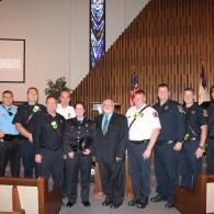 Group of uniformed officers and a suited man posing in a church sanctuary
