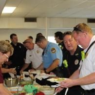 People serving themselves at a buffet in a bright community room, with police officers in uniform among them