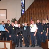 Group of uniformed officers and officials posing indoors beside a church altar.
