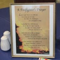 Framed poem titled “A Firefighter’s Prayer” on a blue surface beside a white figurine