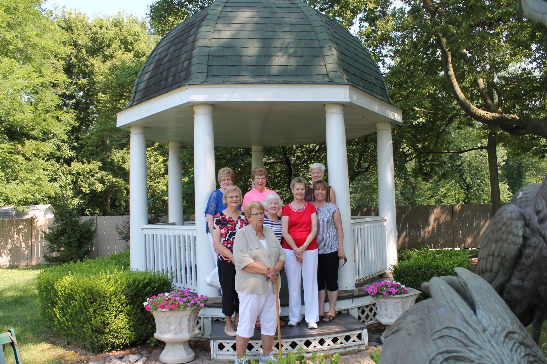 Five people standing in a white gazebo surrounded by flowers and greenery.