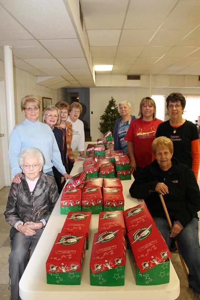 Volunteers gathered around a long table stacked with red holiday gift boxes in a bright room