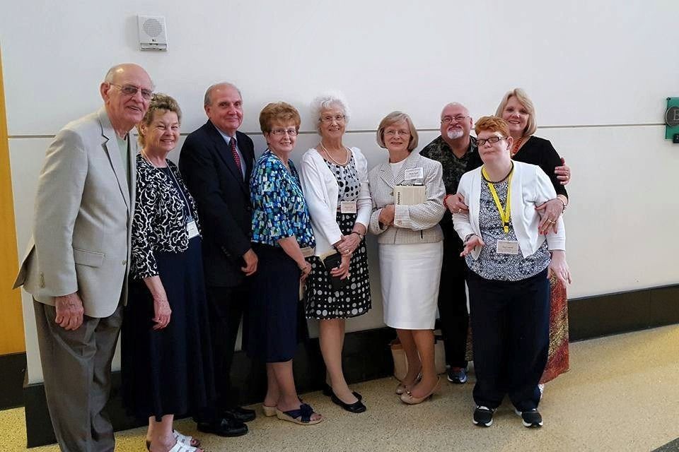 Group of people posing indoors, smiling and holding an award certificate against a white wall.