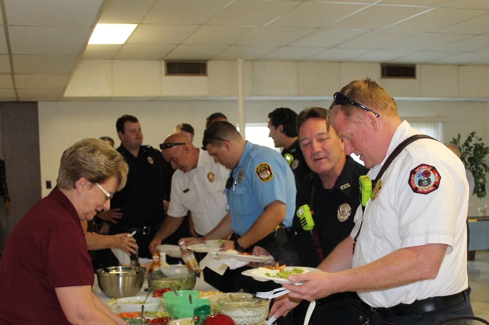 People serving food at a buffet table in a meeting room, with firefighters and officers waiting in line