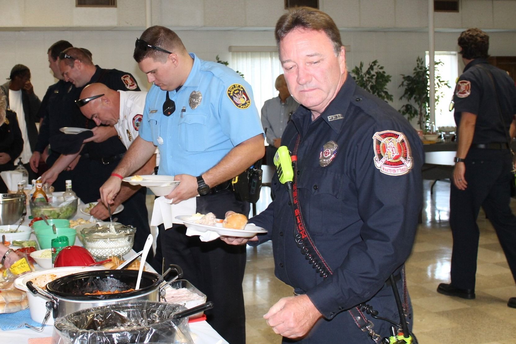 Firefighters in uniform serving themselves food at a buffet table indoors
