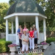 Five people standing in a white gazebo with a green domed roof in a garden.
