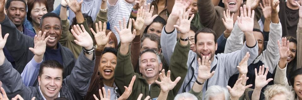 Crowd of smiling people waving their hands toward the camera outdoors