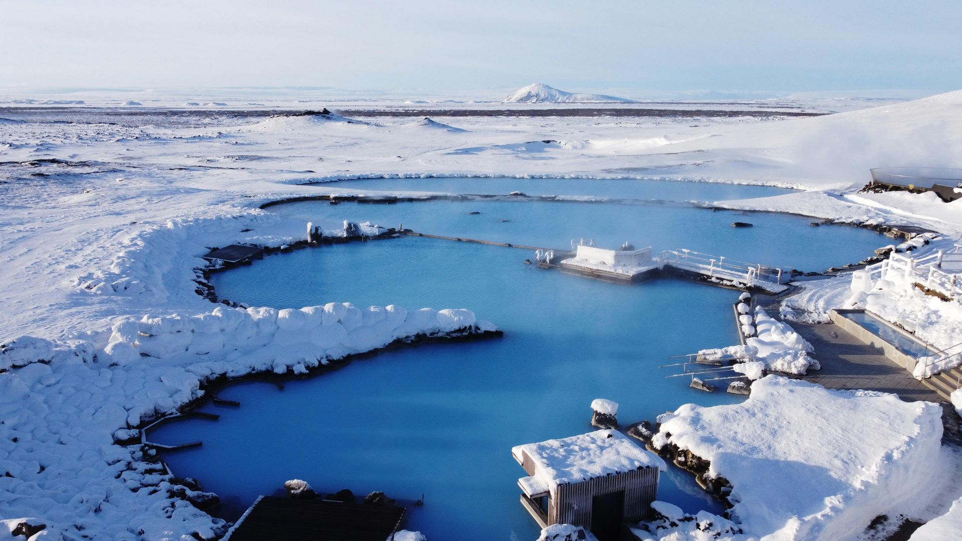 Snow-covered landscape with turquoise geothermal pools in Iceland, building covered in snow.