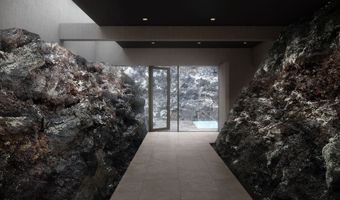 Hallway flanked by dark, textured rock walls, leading to a glass door revealing a pool and outdoor view.