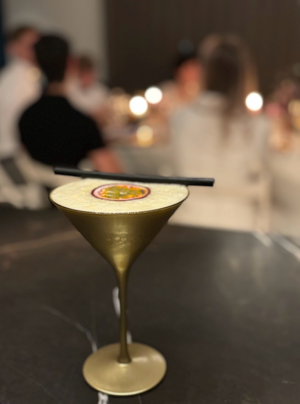 Een cocktail in een martiniglas met garnering, geserveerd op een tafel tegen een zacht vervaagde loungeachtergrond.