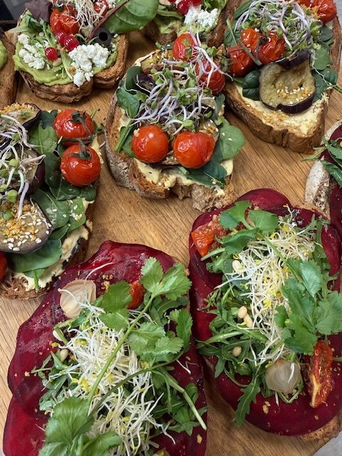 Diverse bruschetta, gegarneerd met tomaten, bladgroenten en taugé, geserveerd op een houten plank.