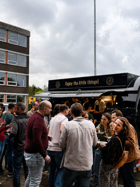 Een menigte had zich verzameld buiten een zwarte eetkraam onder een bewolkte hemel tijdens een evenement in de openlucht.