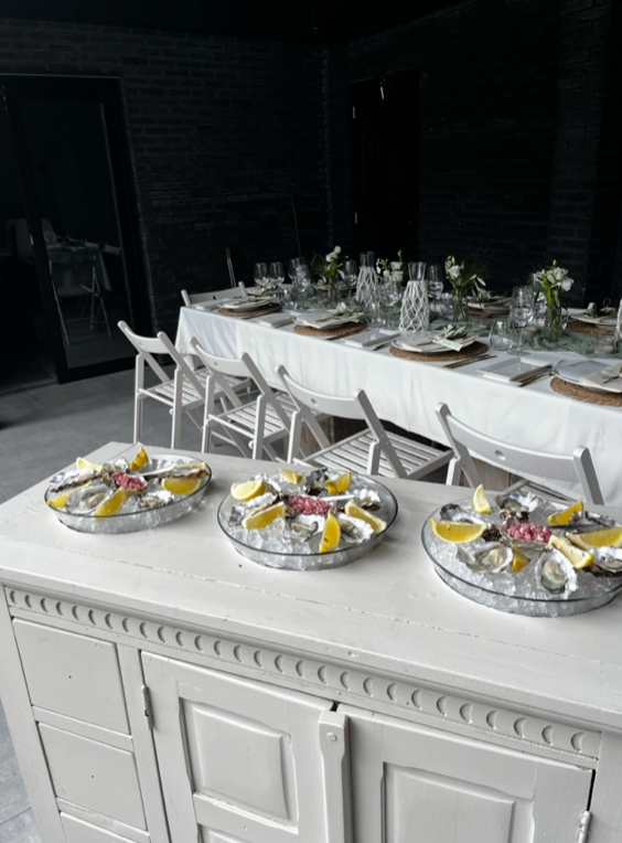 Een buffettafel voor buiten, gedekt met een wit tafelkleed, zilveren schalen met eten en glaswerk