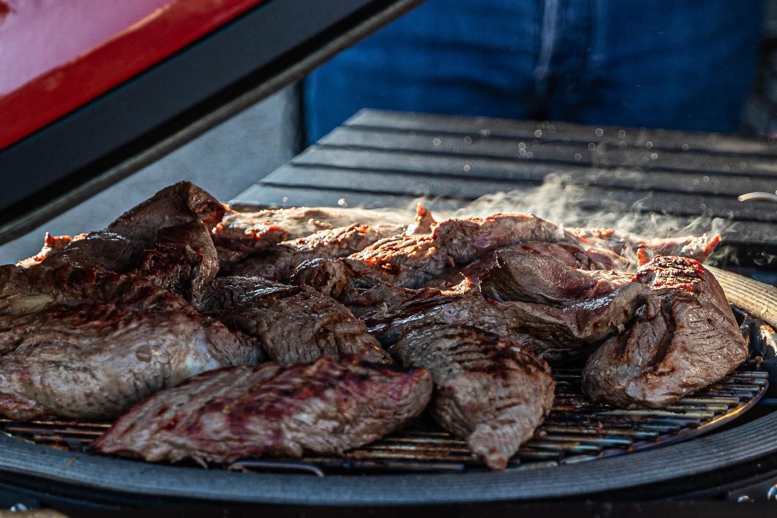 Gegrilde steaks die sissen op een barbecuerooster boven een open vlam.