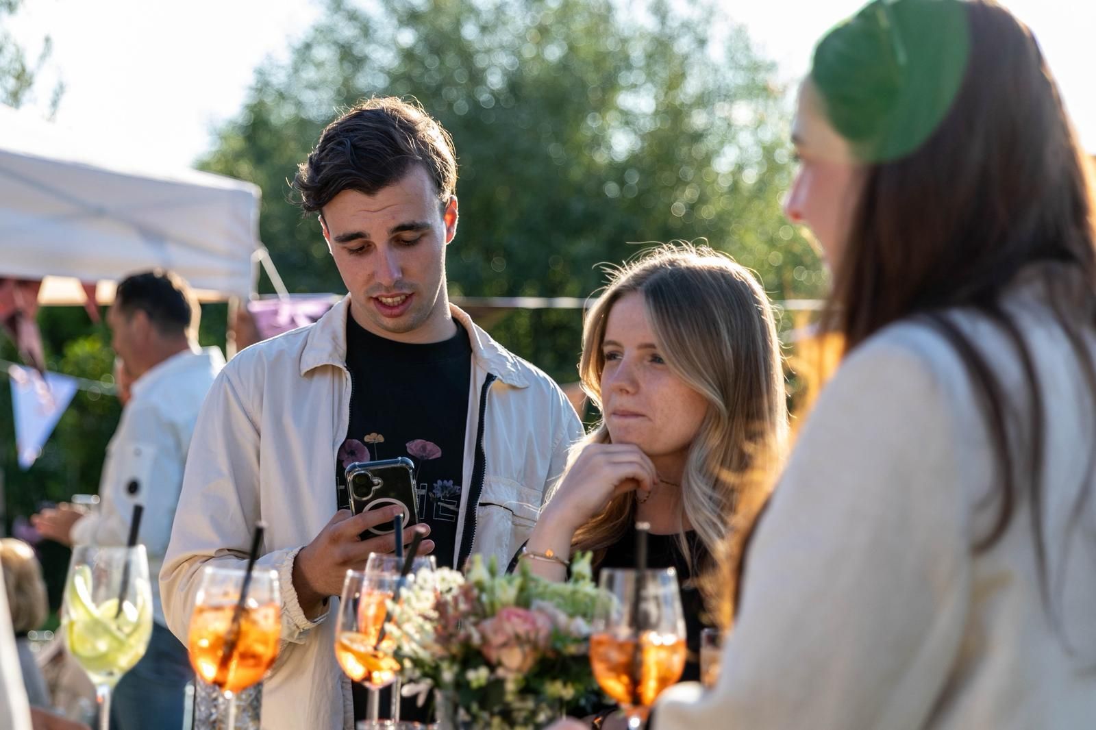 Mensen die gezellig met elkaar praten tijdens een buitenbijeenkomst met drankjes en lichtslingers.