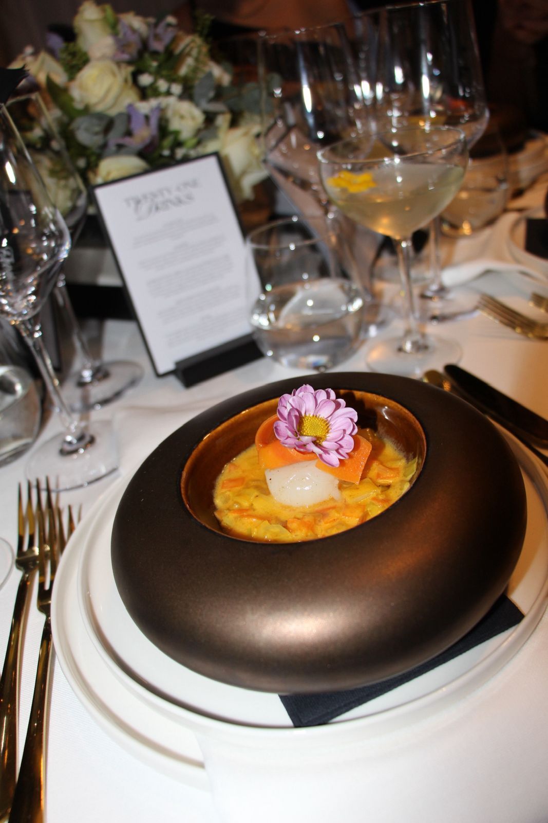 Elegant opgemaakt voorgerecht met roze garnering op een eettafel onder de warme verlichting van het restaurant.