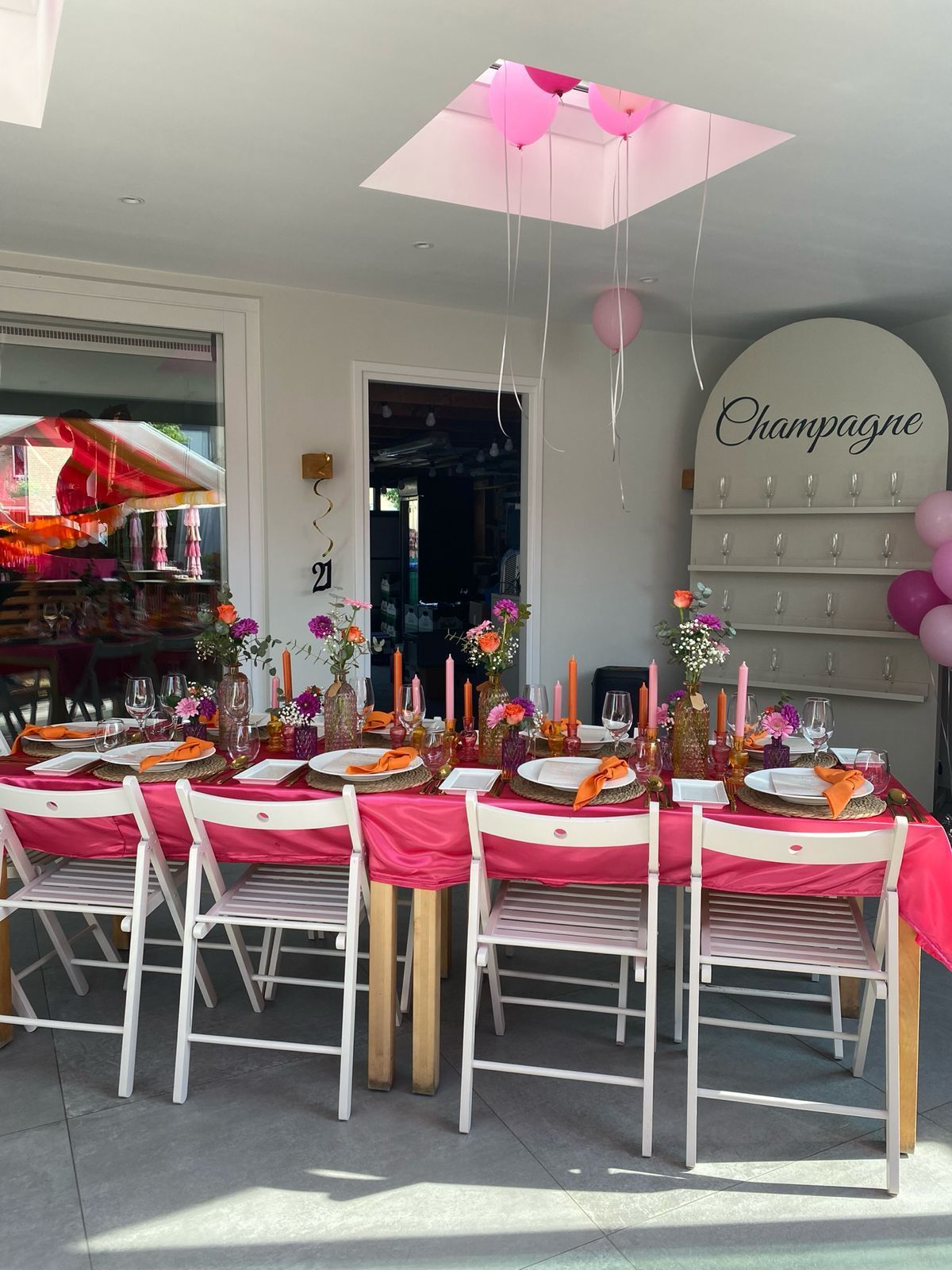 Een feesttafel in roze thema in een lichte kamer, met witte stoelen, ballonnen