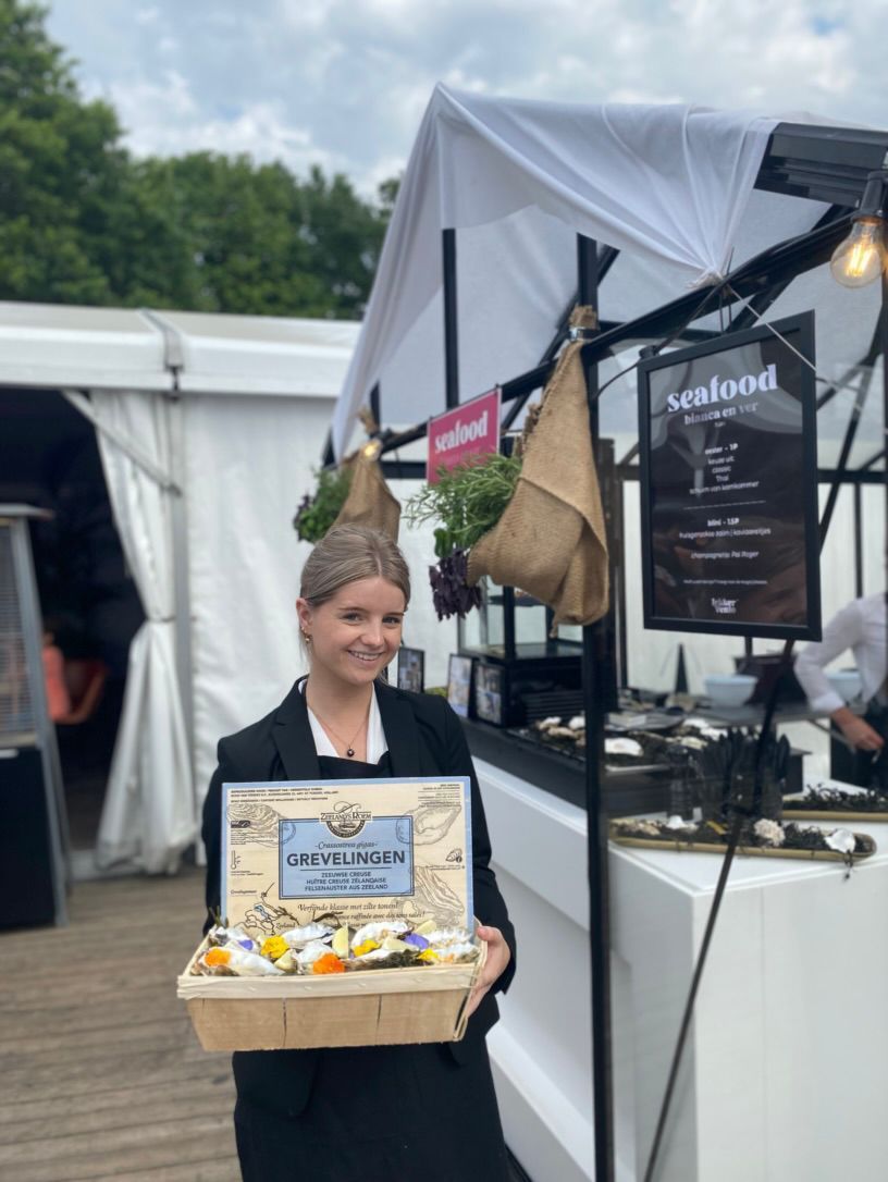 Vrouw met een prijsplaquette voor een zwart-wit marktkraam buiten.